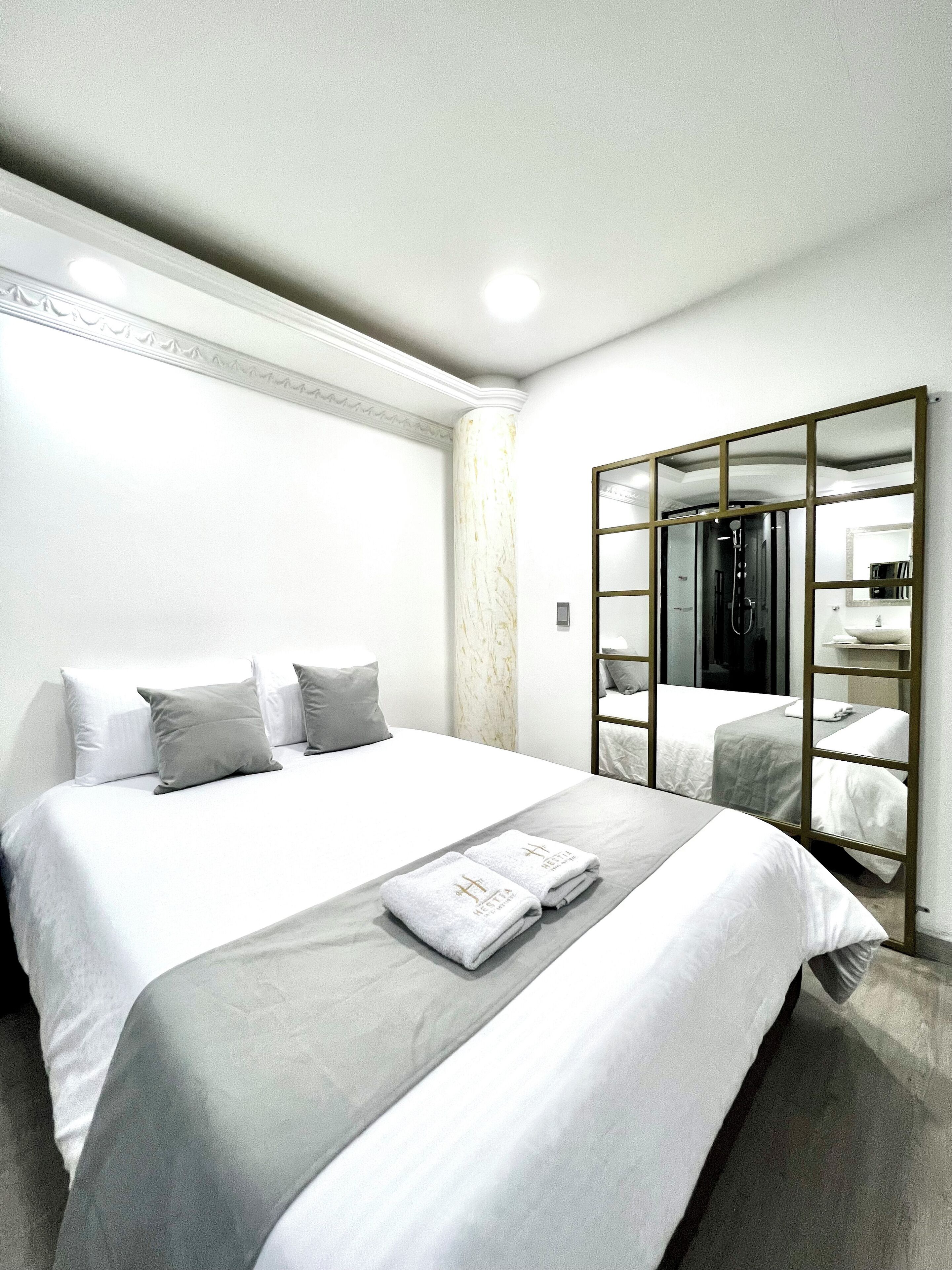 A hotel room with a large bed, a wardrobe with a mirror, and a small bathroom visible through the mirror.