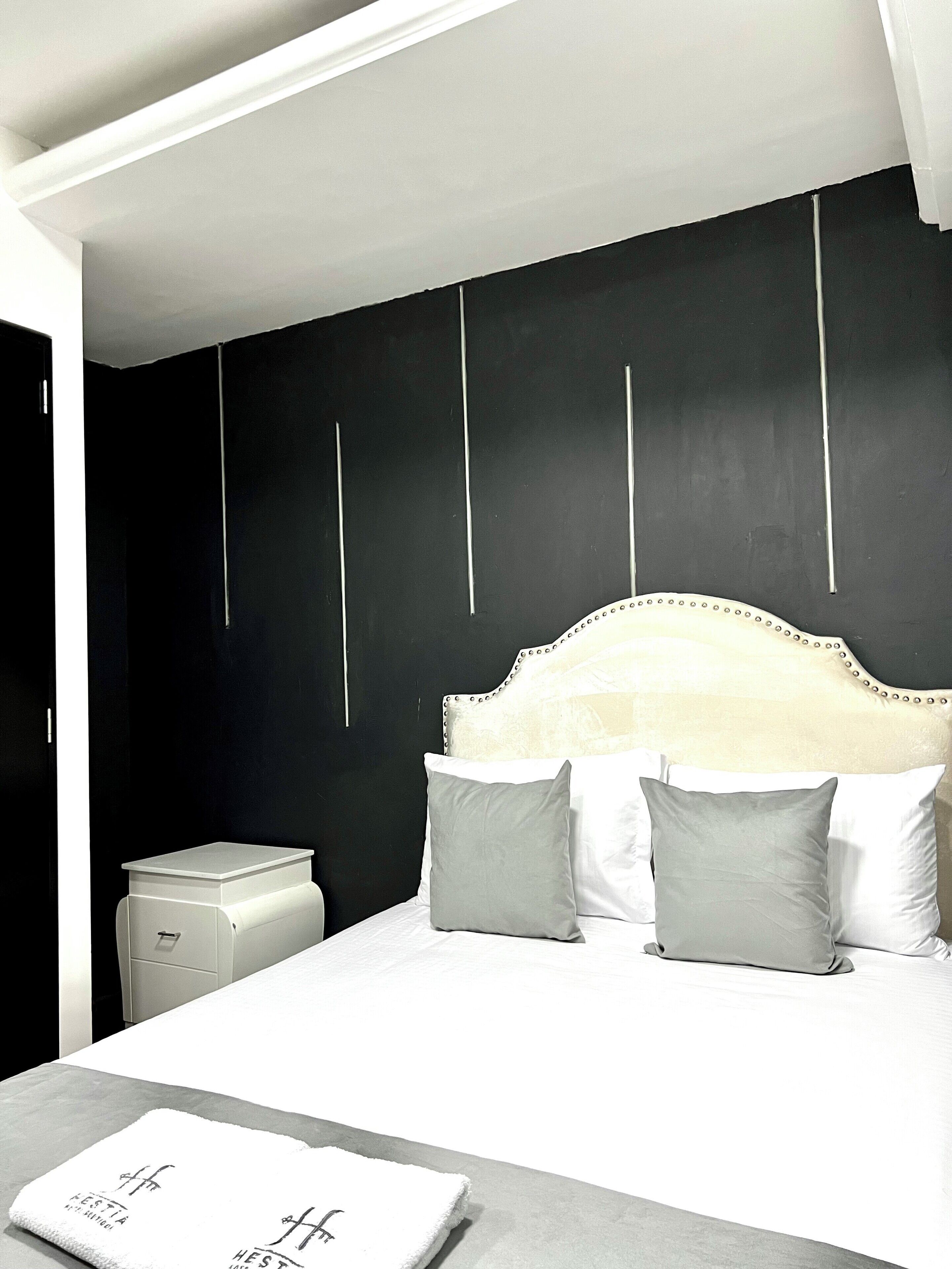 A modern bedroom with a white bed, two pillows, a nightstand, and a small white cabinet.