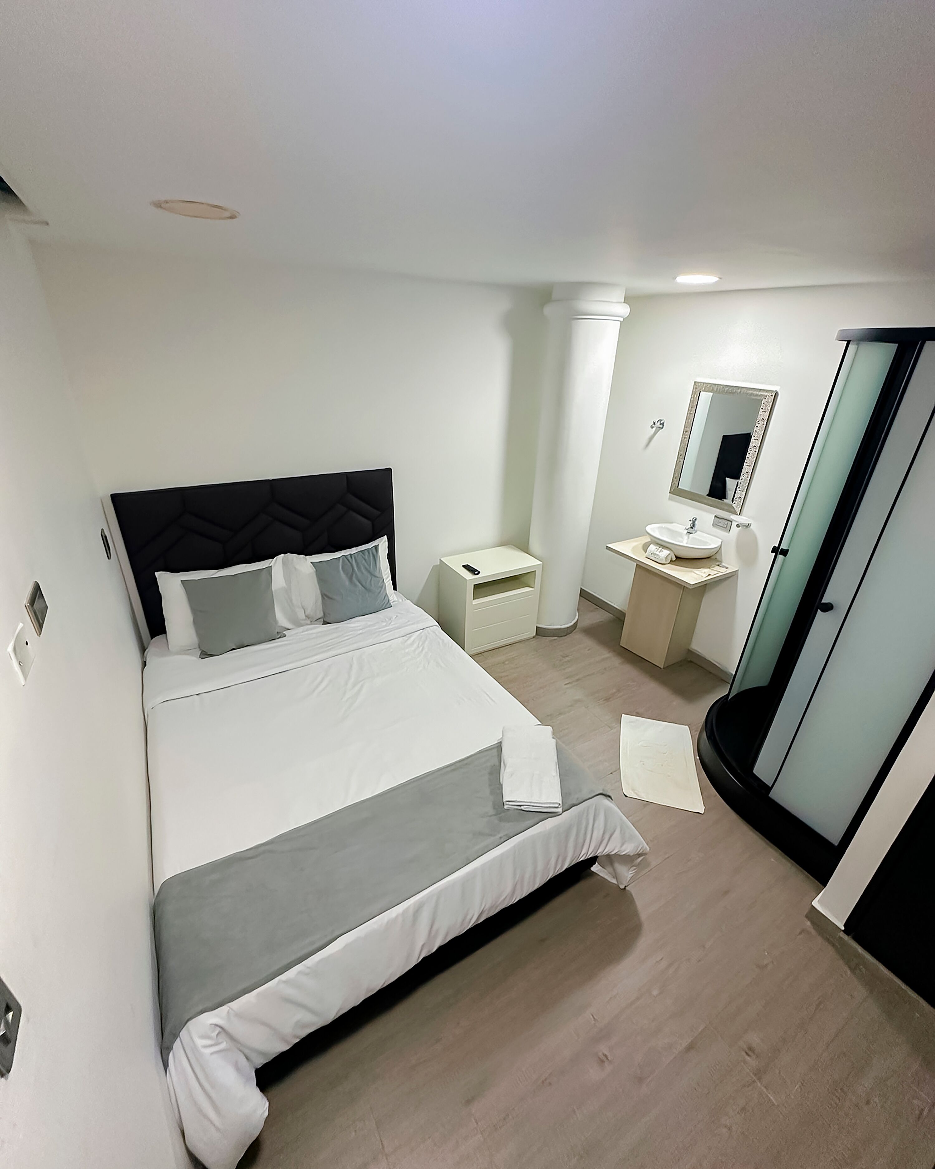 A modern bedroom with a bed, bedside table, and a bathroom with a sink and mirror.