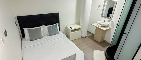 A modern bedroom with a bed, bedside table, and a bathroom with a sink and mirror.