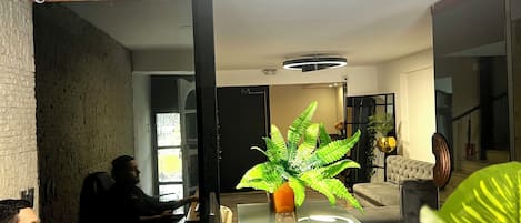 Moderni toimistotila, jossa henkilö työskentelee työpöydän ääressä, ja tilassa on myös ruukussa oleva kasvi sekä ainutlaatuinen kattovalaisin.