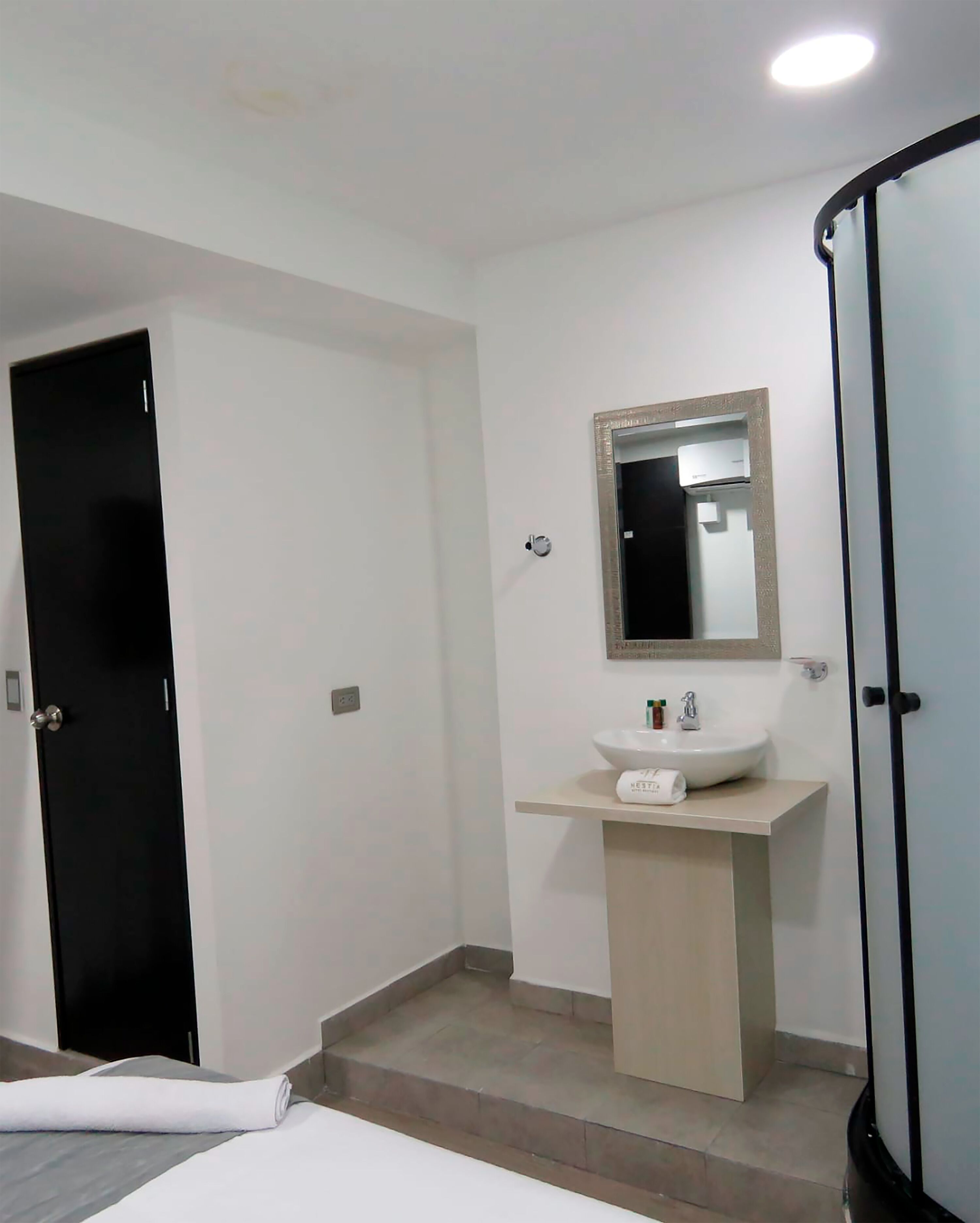 A bathroom with a black door, a white sink with a mirror above it, and a shower area.