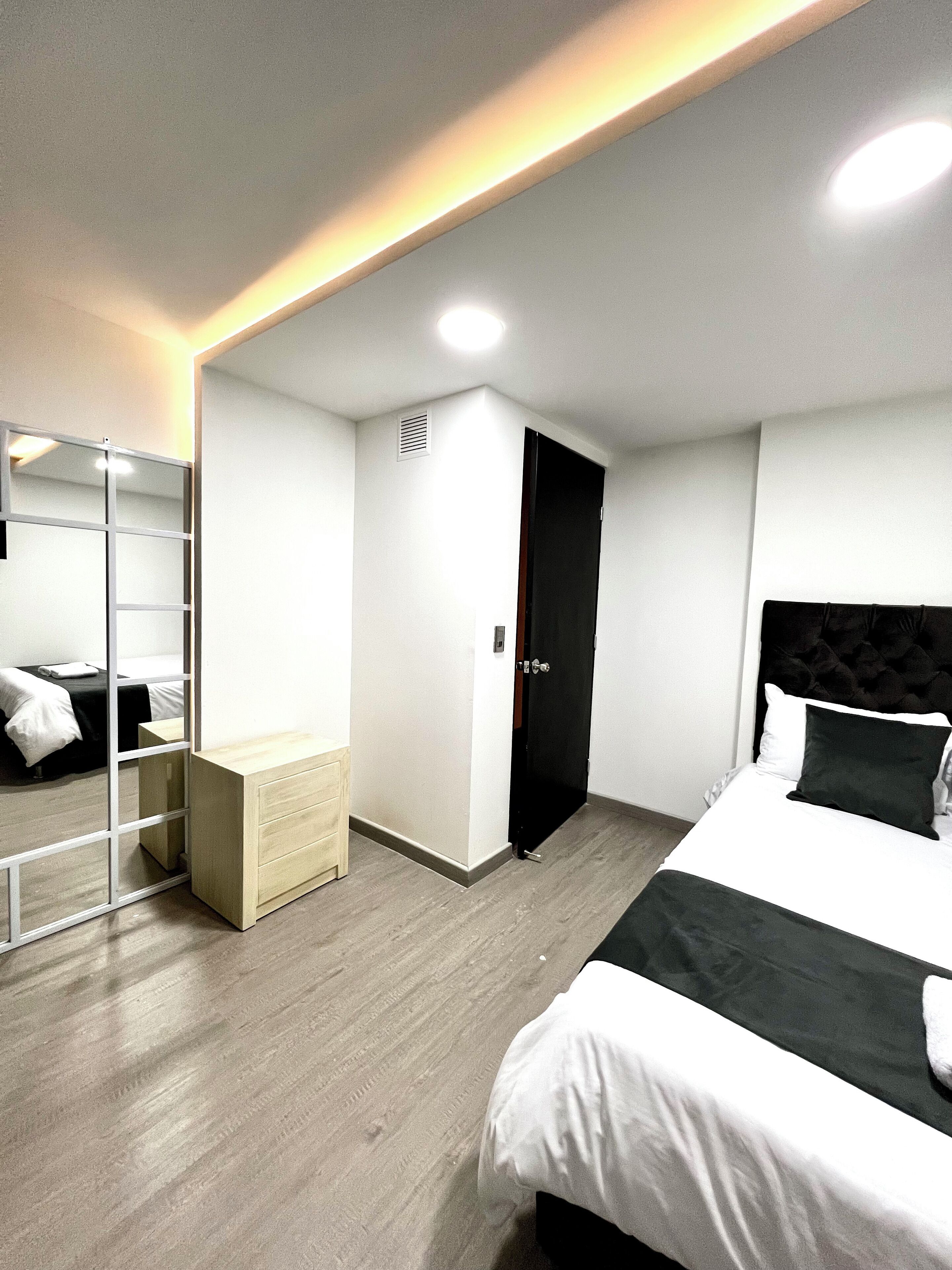 A modern hotel room with a bed, a wardrobe, a mirror, and a bedside table.
