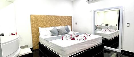 A modern hotel room with a large bed, a bathroom, and a mirror.