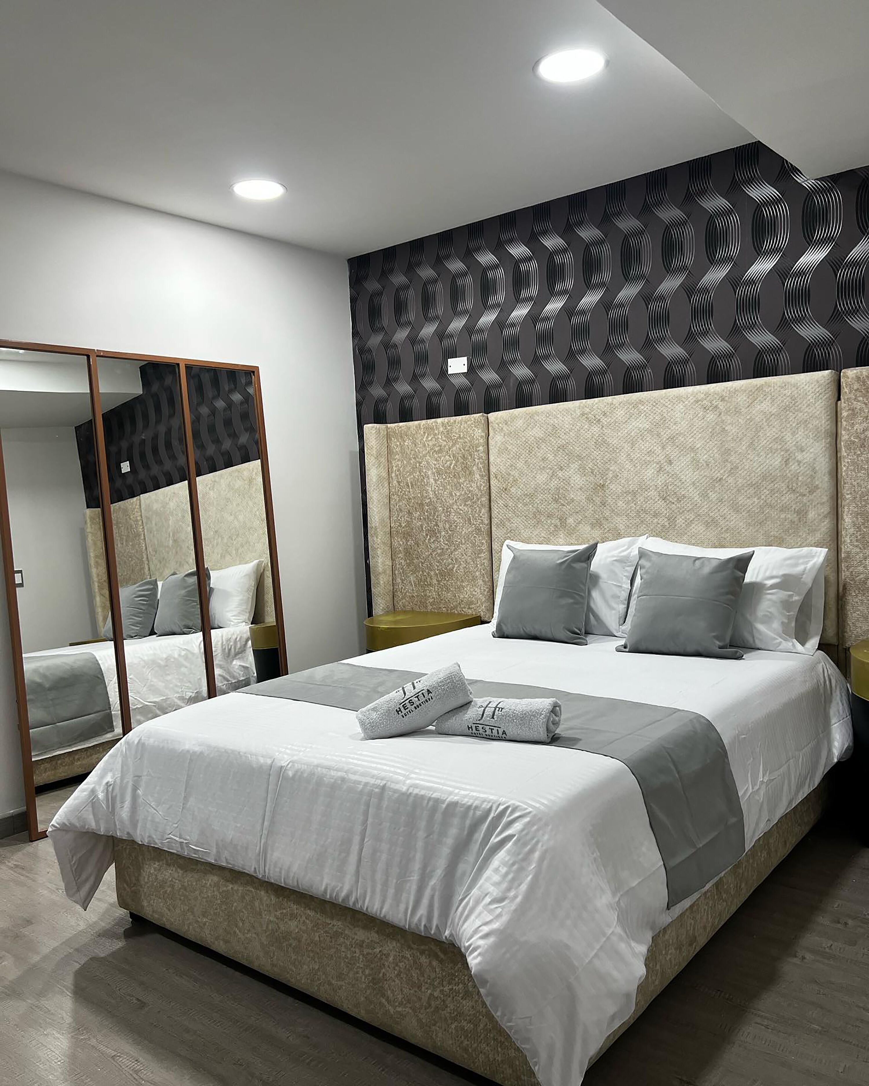 A modern bedroom with a large bed, a wardrobe, and a patterned wall.