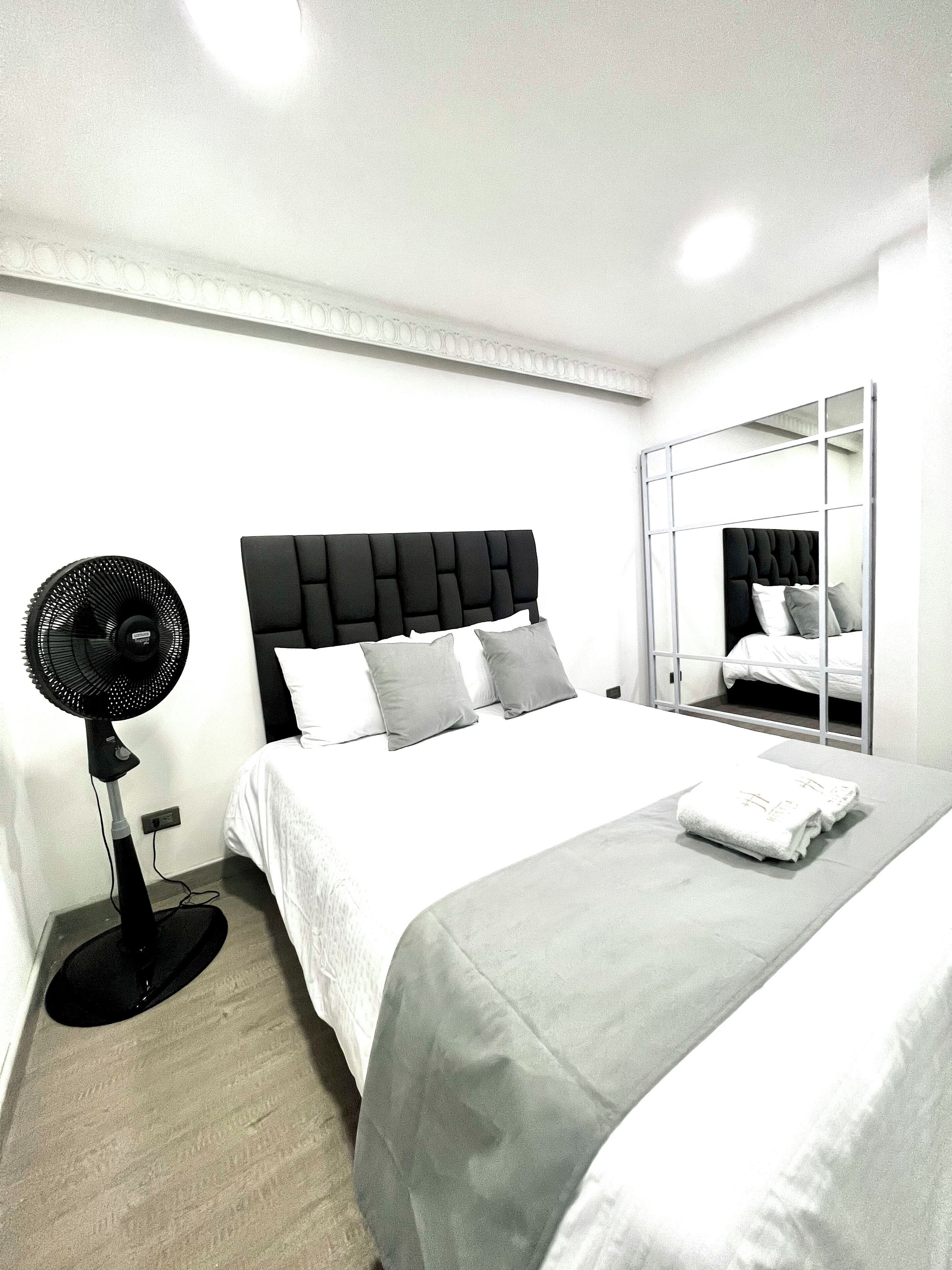 Hotellihuone, jossa on sänky, lattiatuuletin ja peili.