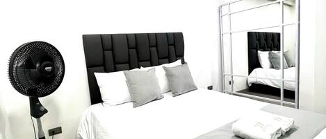 A hotel room with a bed, a standing fan, and a mirror.
