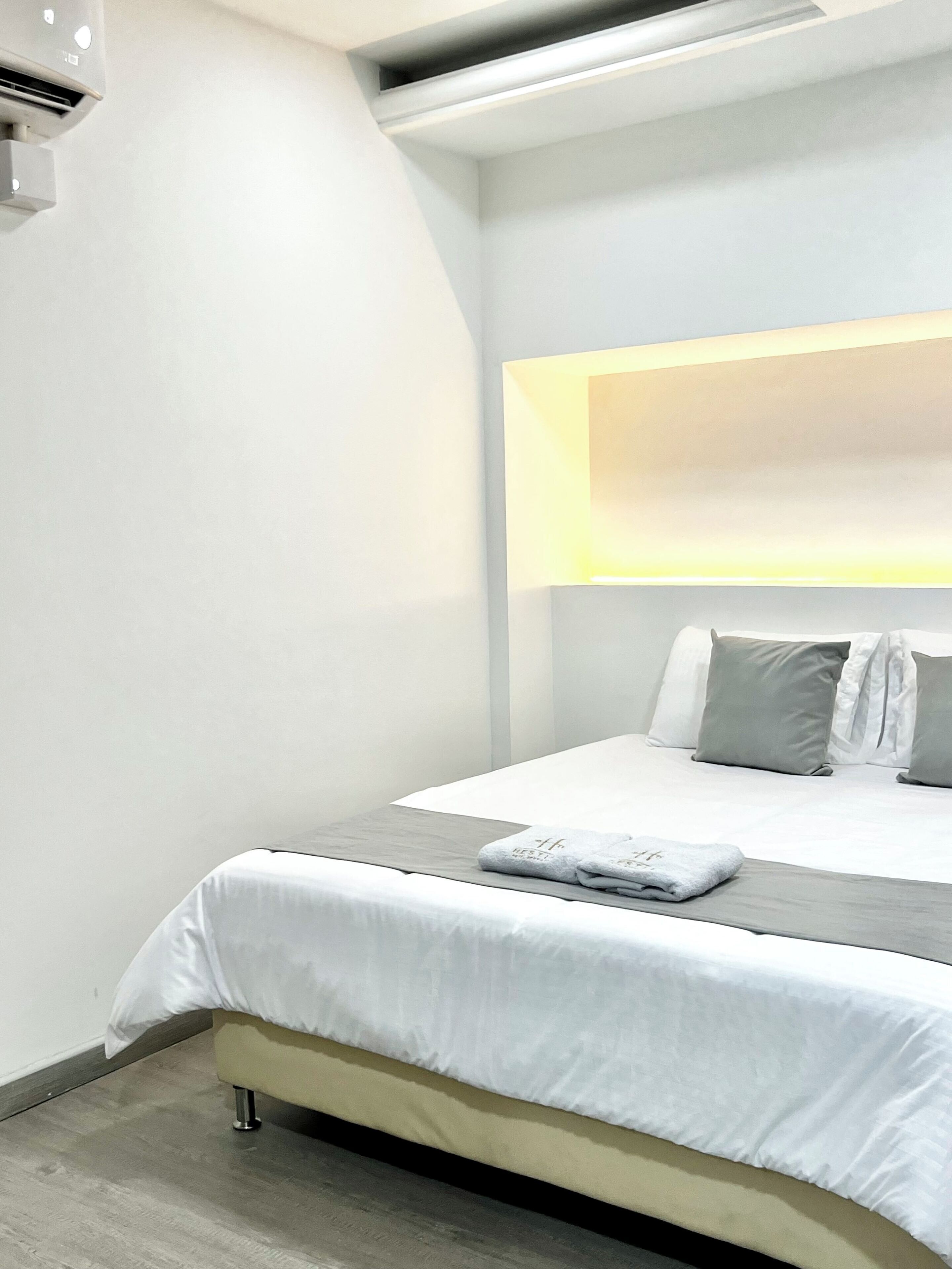 A modern hotel room with a bed, a bedside table, and a wall-mounted light fixture.