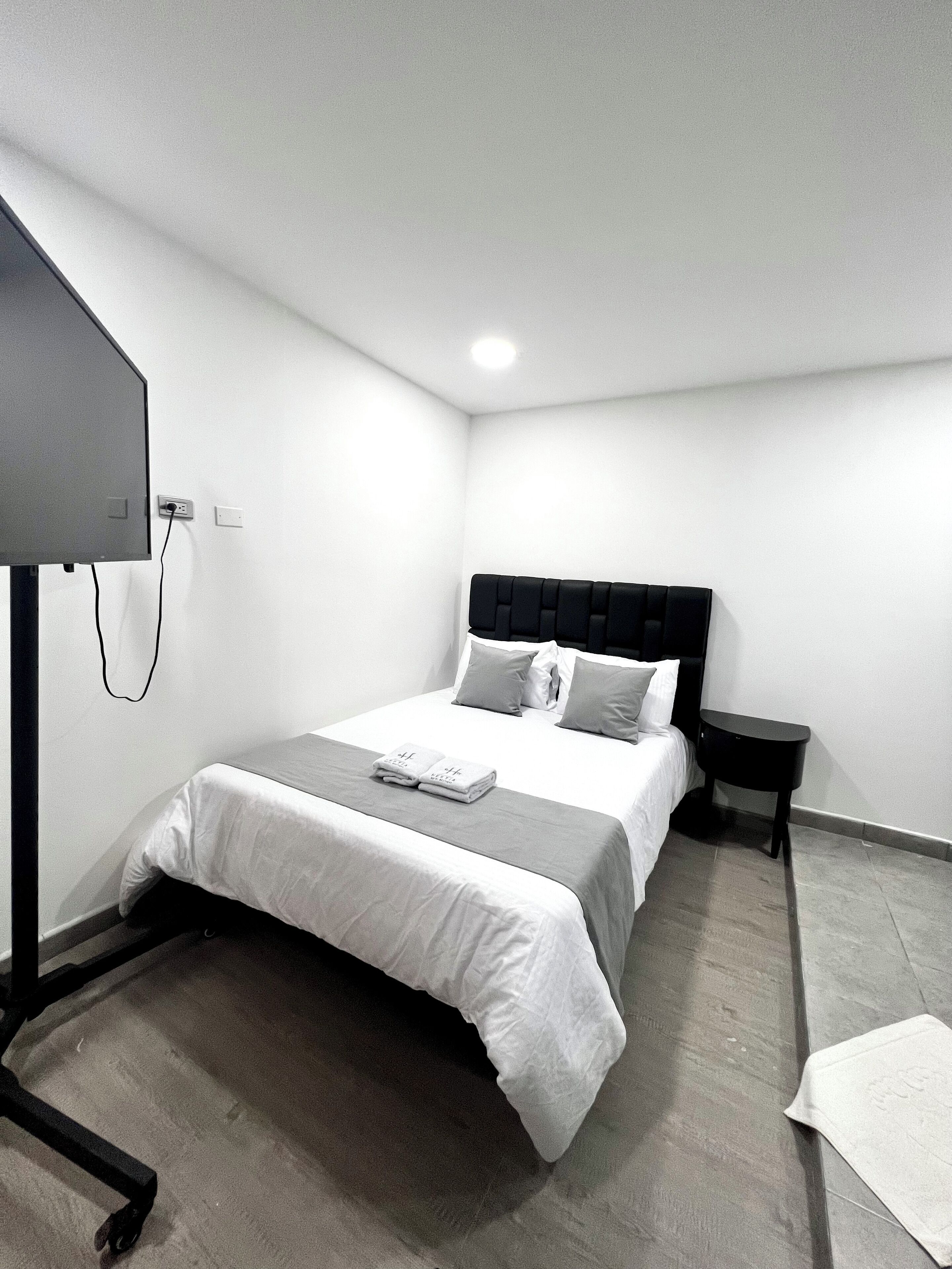 Une chambre d’hôtel moderne avec un lit bien fait, une petite table de chevet et un téléviseur à écran plat fixé au mur.