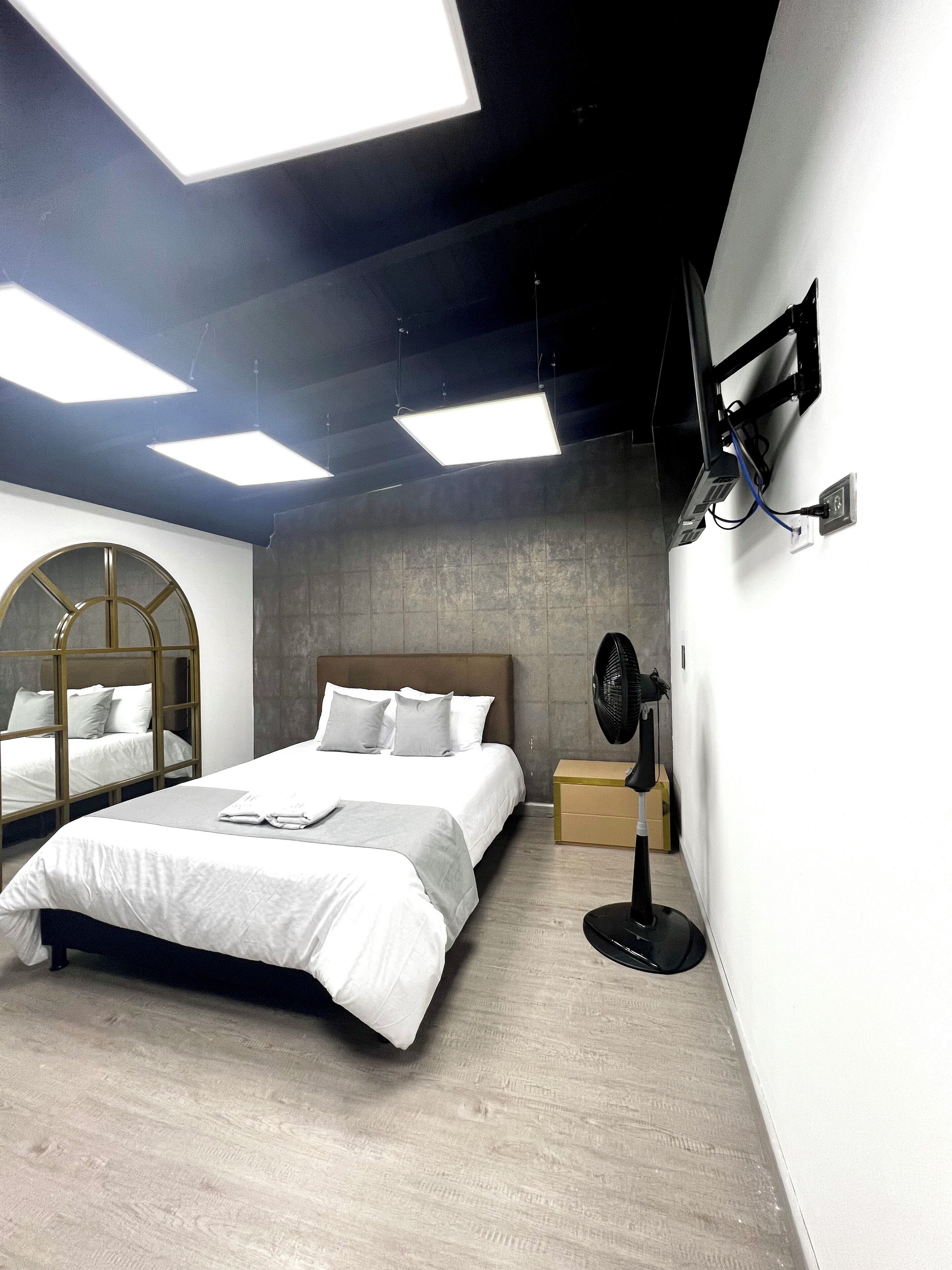Um quarto moderno com uma cama grande, um ventilador de chão e uma TV fixada na parede.
