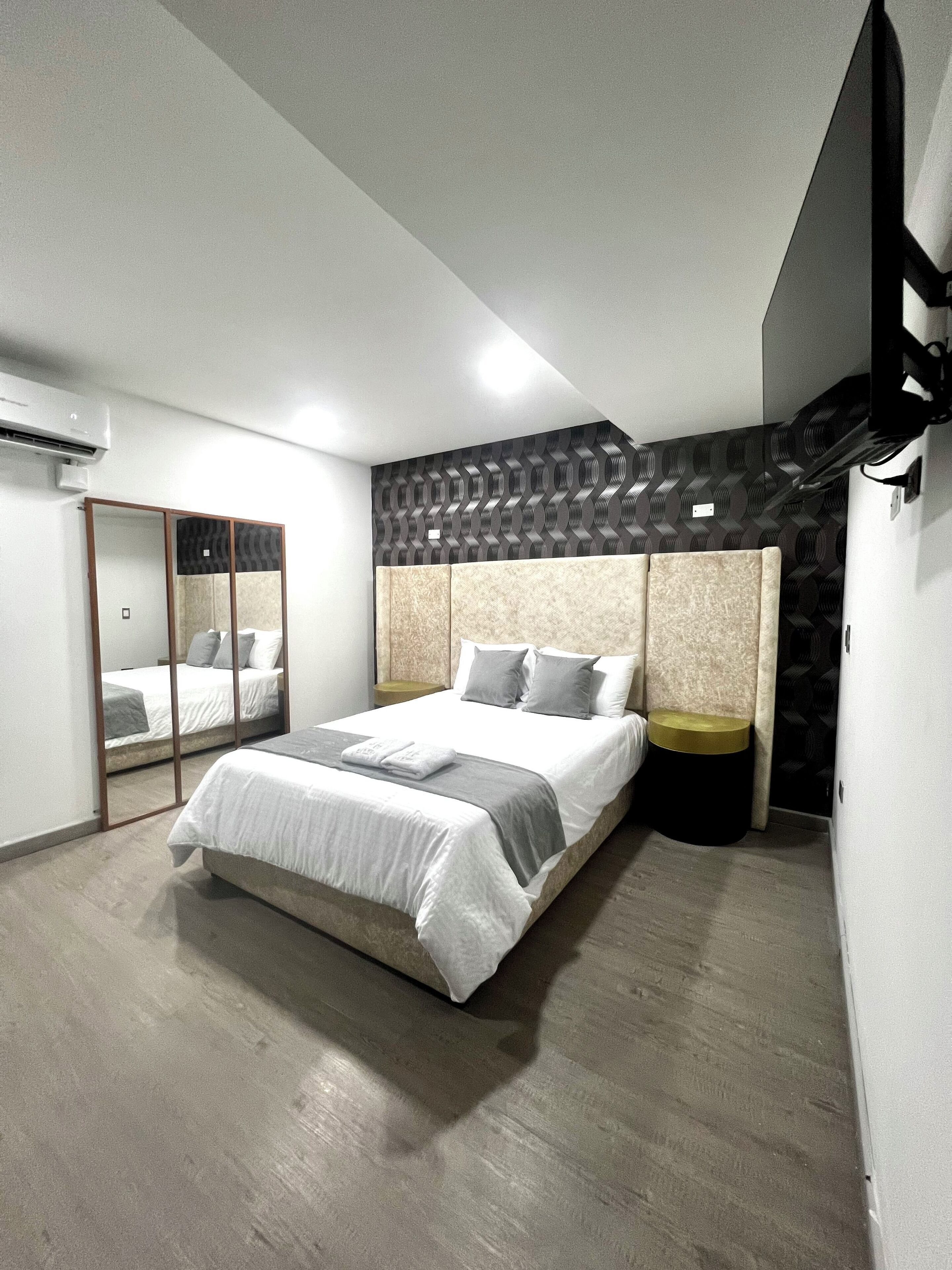 A modern bedroom with a large bed, a mirror, and a patterned wall.