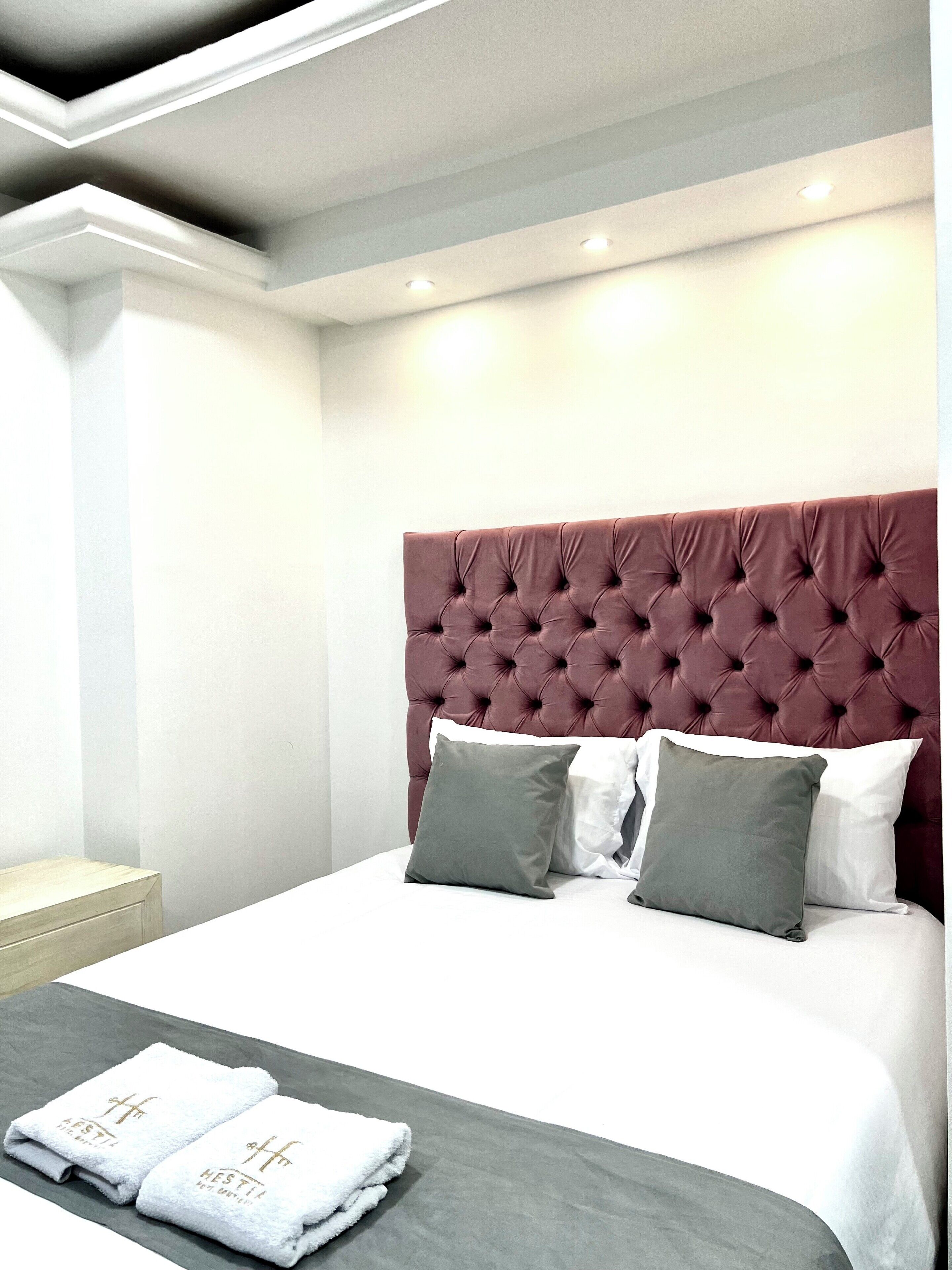 A neatly made bed with a tufted headboard, two pillows, and two folded towels on a gray bedspread.