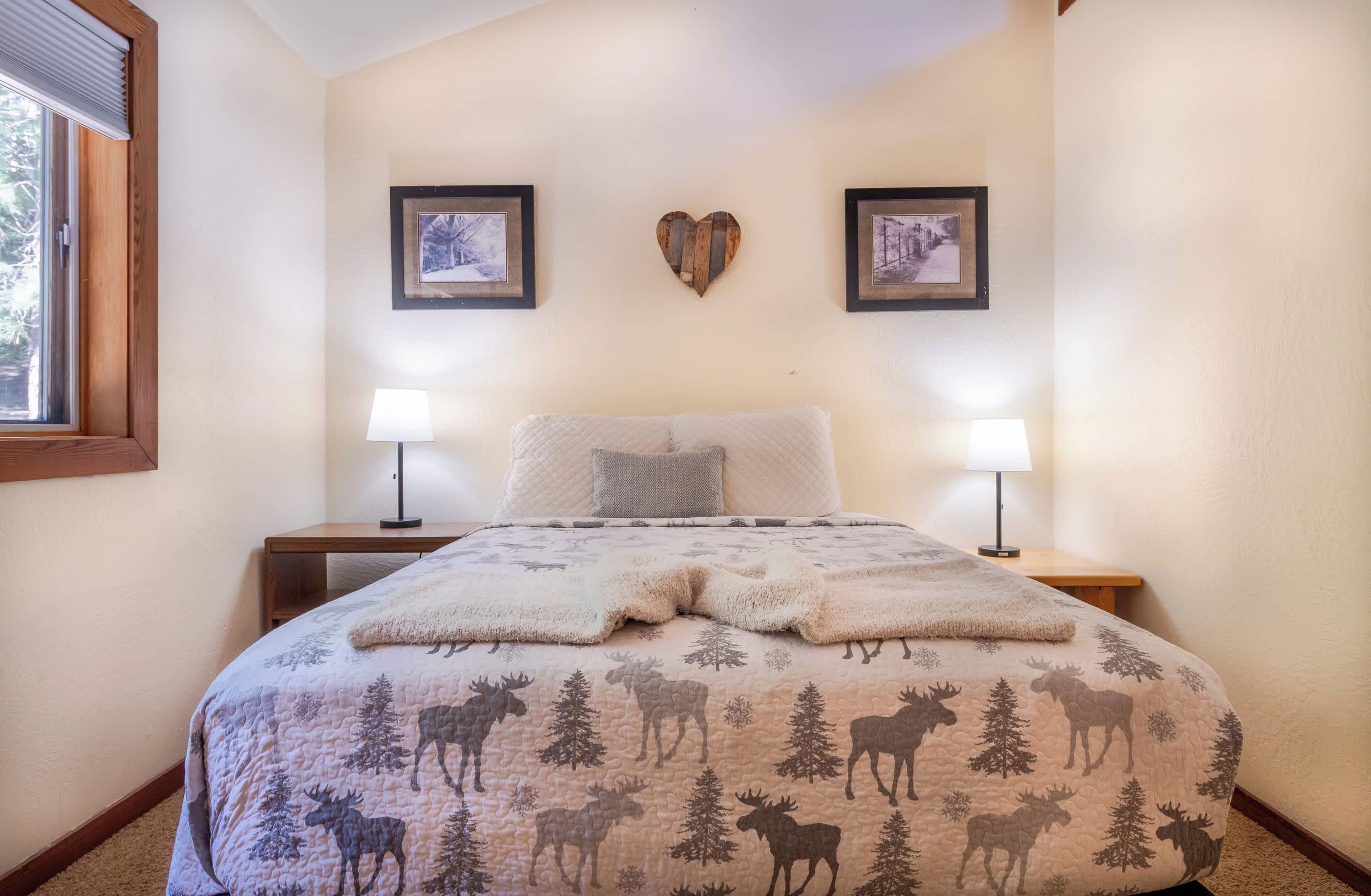 A bedroom with a bed, two bedside lamps, a window, and two framed pictures on the wall.