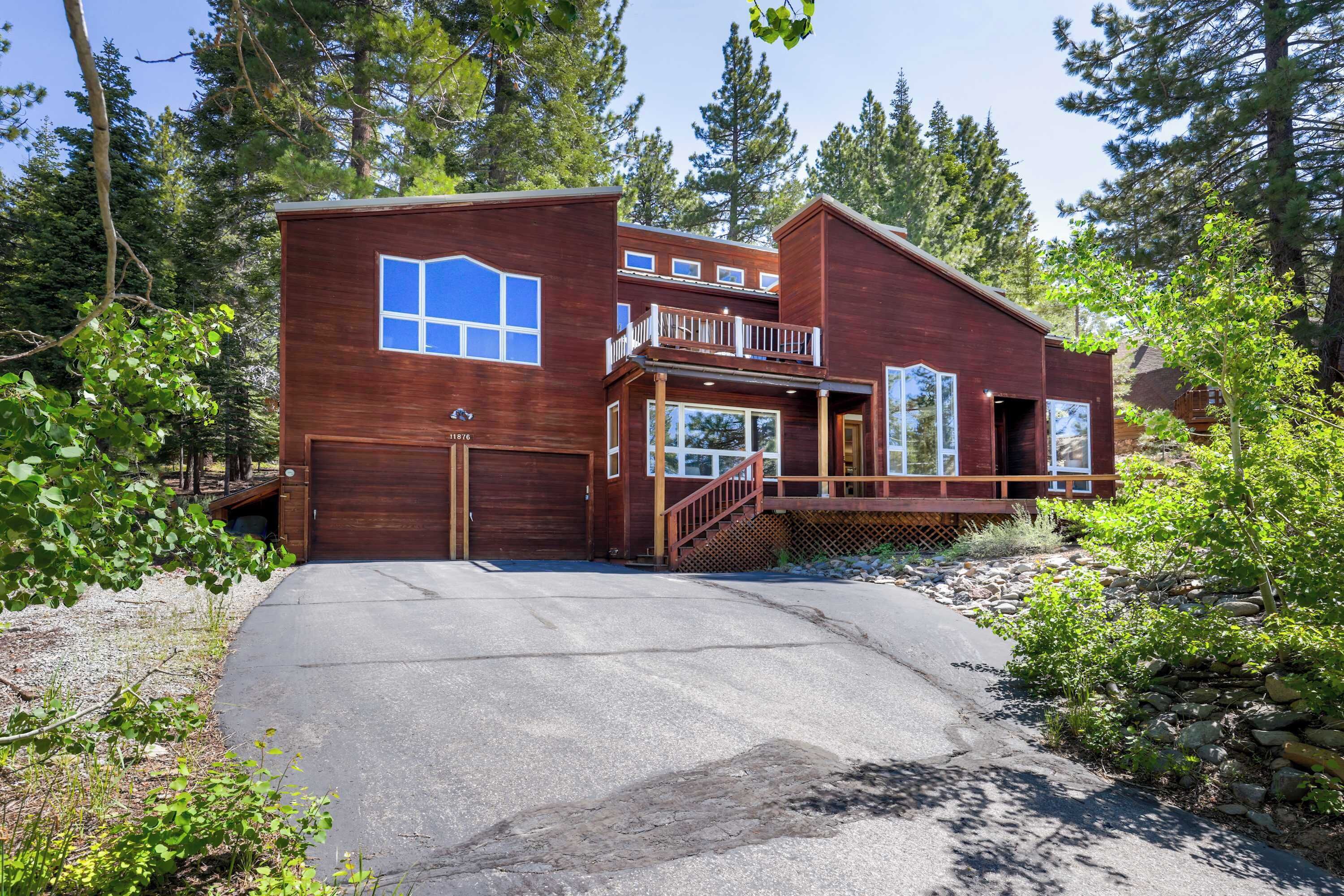 A two-story wooden cabin with a balcony, a garage, and a stone pathway leading to the entrance.
