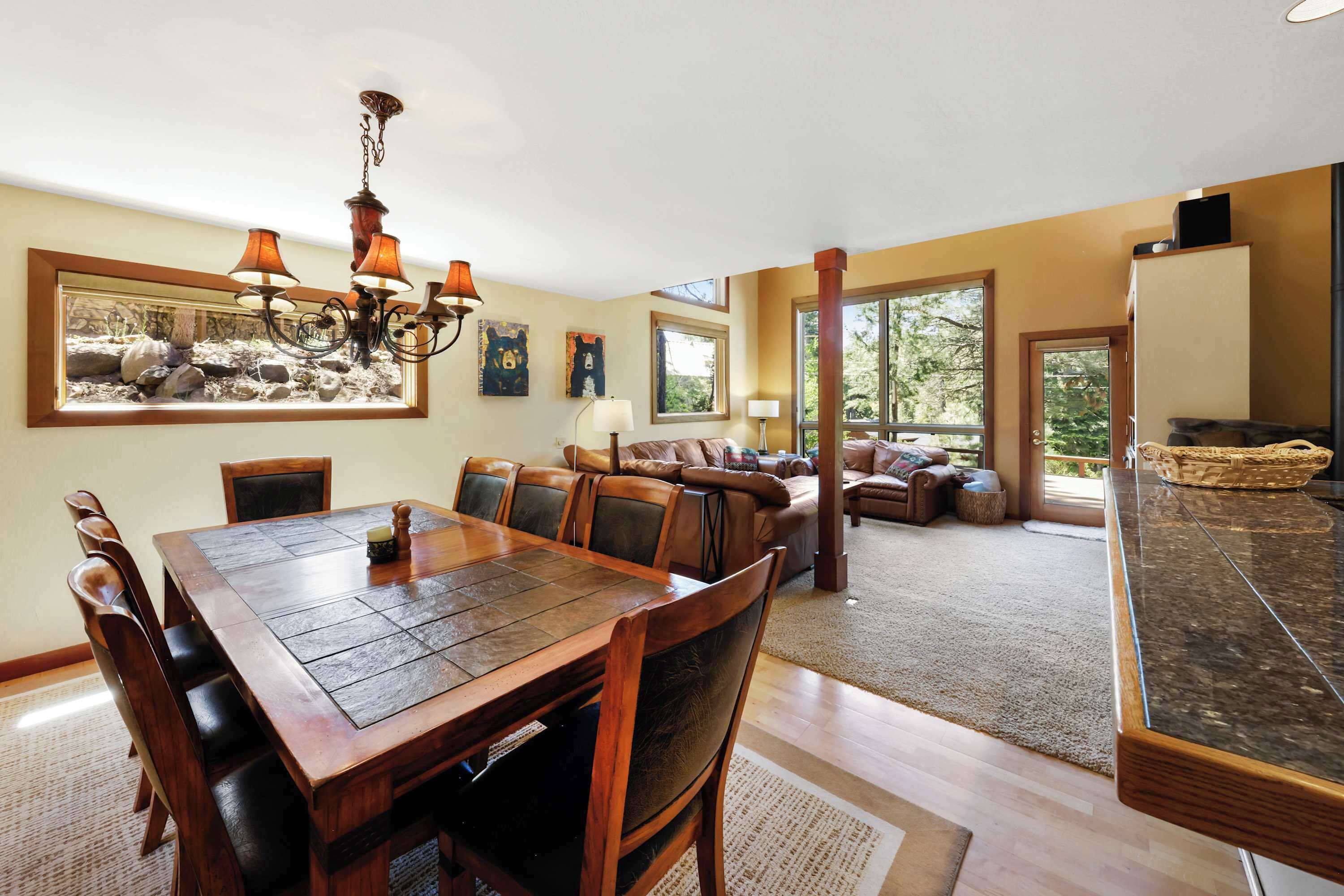 A spacious living room with a large wooden dining table, comfortable seating, and a view of the outdoors.