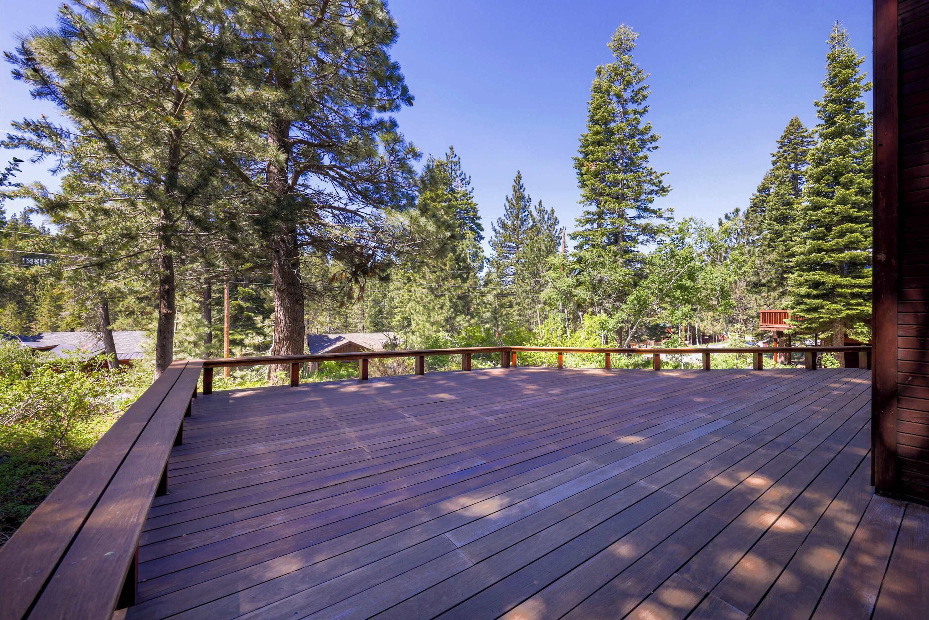 A wooden deck with a railing, surrounded by tall trees and a clear sky.