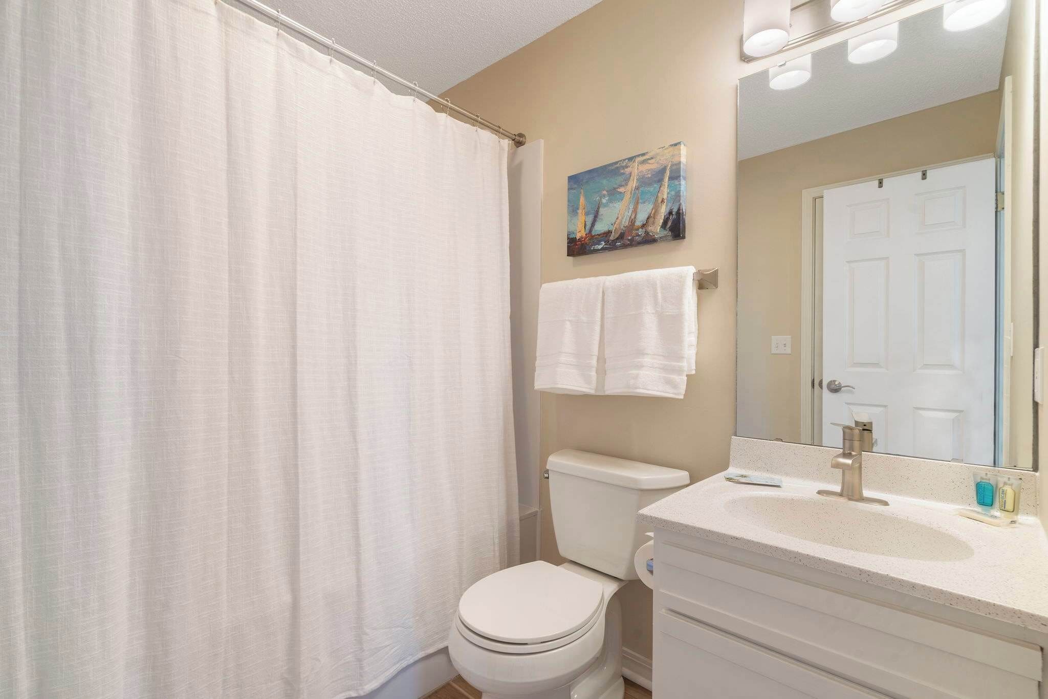 A bathroom with a white toilet, a sink with a mirror, and a shower curtain.