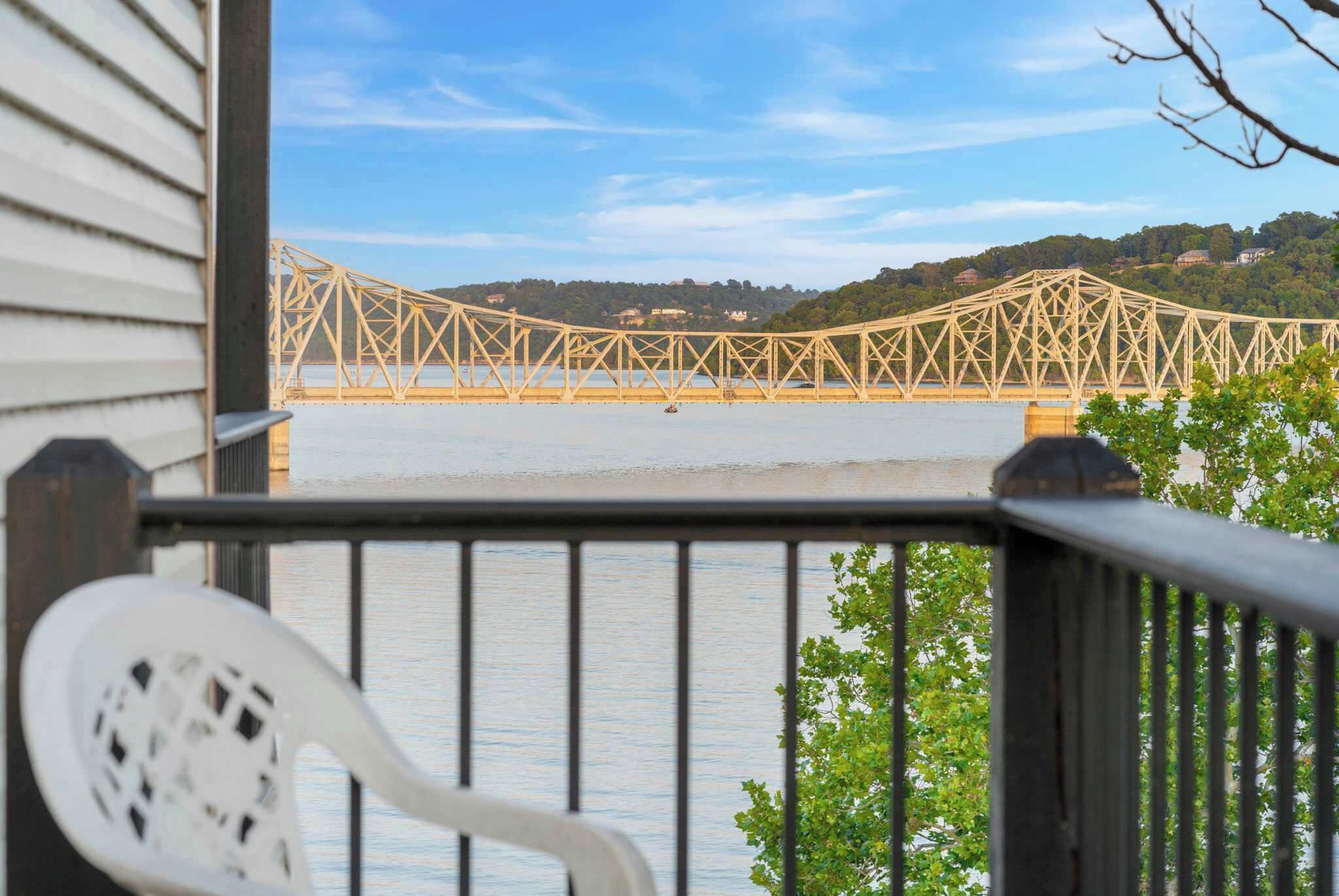 A view of a suspension bridge over a body of water, with a railing and a chair in the foreground.