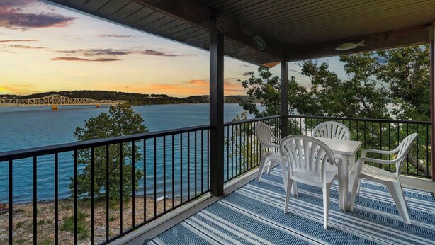 A covered outdoor area with a view of a bridge over water, a table with chairs, and a railing. - Enjoy Lakeside Fun Lakeview At Table Rock! (Kimberling City)