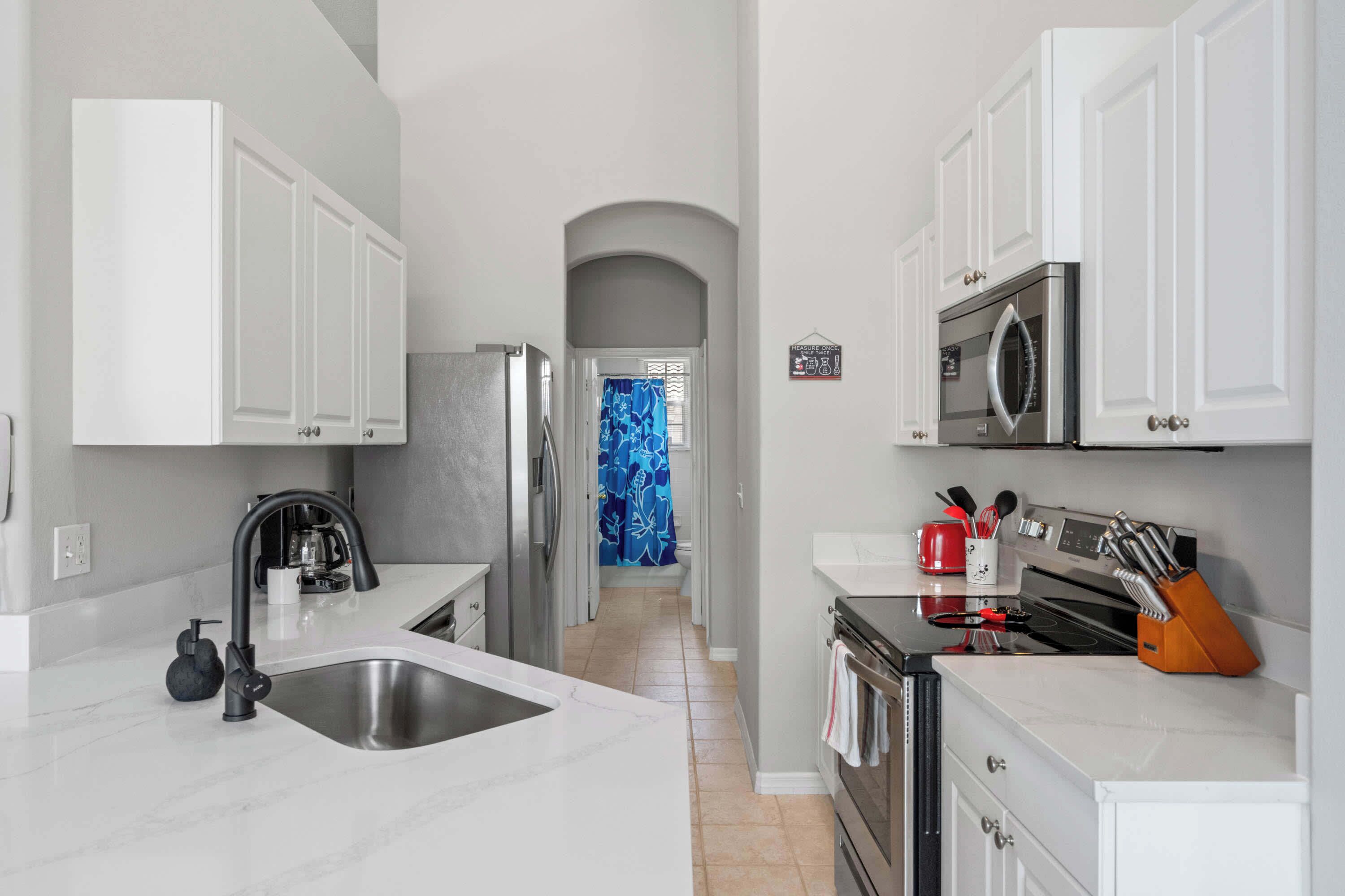 A modern kitchen with white cabinetry, a stainless steel sink, a microwave, and a stove.