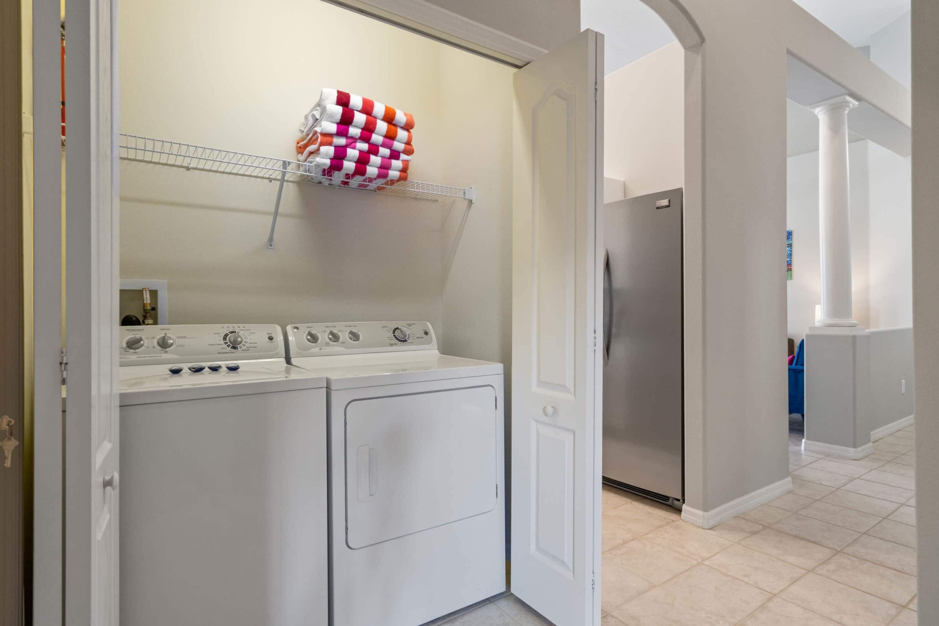A laundry area with a washer and dryer, a metal shelf with folded towels, and a refrigerator.