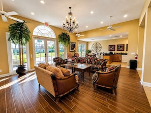 A spacious living room with a large dining table, comfortable seating, and a view of the outdoors through a glass door. - Magical Memories Villa Private Pool! (Davenport)