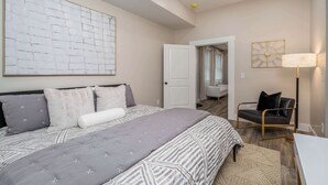 A modern bedroom with a large bed, a bedside table, a chair, and a lamp. - Lee Street Lodge (Covington)