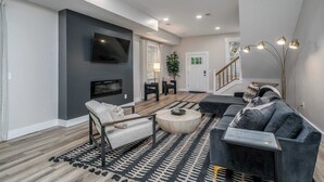 A modern living room with a sofa, armchair, and coffee table, a flat-screen TV mounted on the wall, and a staircase leading to another level. - Lee Street Lodge (Covington)