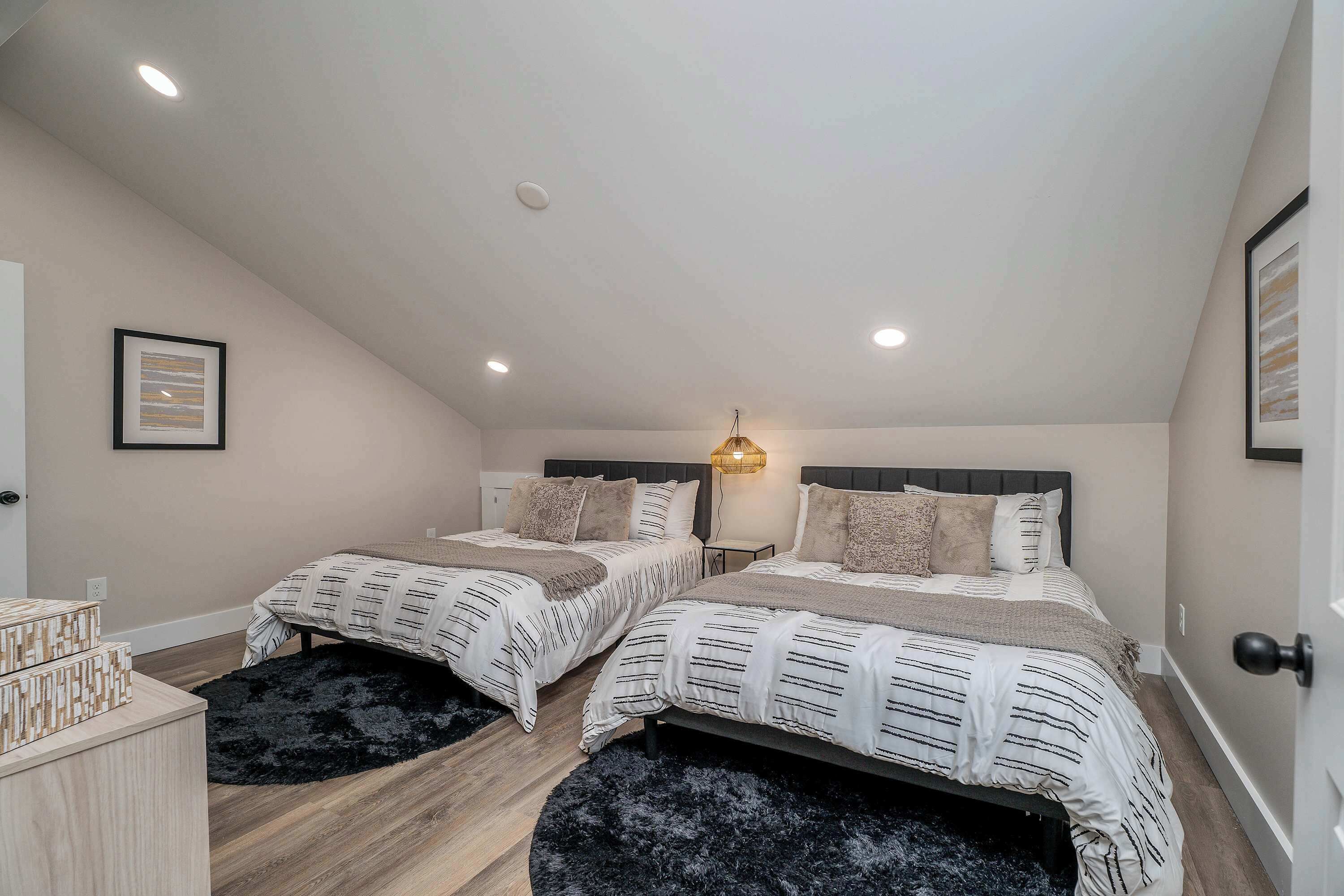 A bedroom with two beds, a black furry rug, a wooden dresser, and a wall-mounted light fixture.