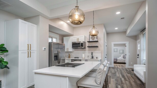 A modern kitchen with white cabinetry, a central island, stainless steel appliances, and pendant lighting. - Lee Street Lodge (Covington)