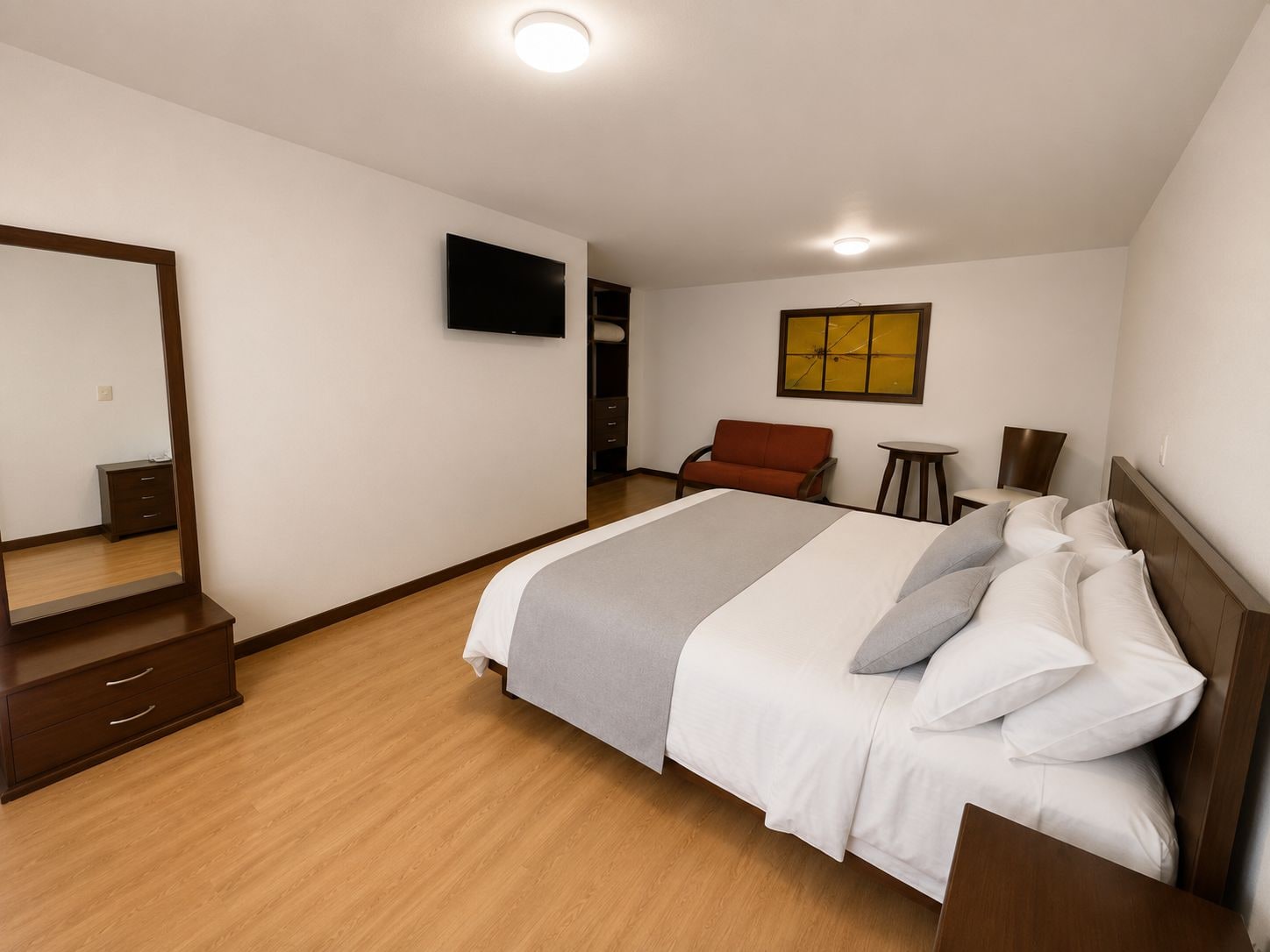 A hotel room with a bed, a mirror, a TV, a sofa, and a small table.