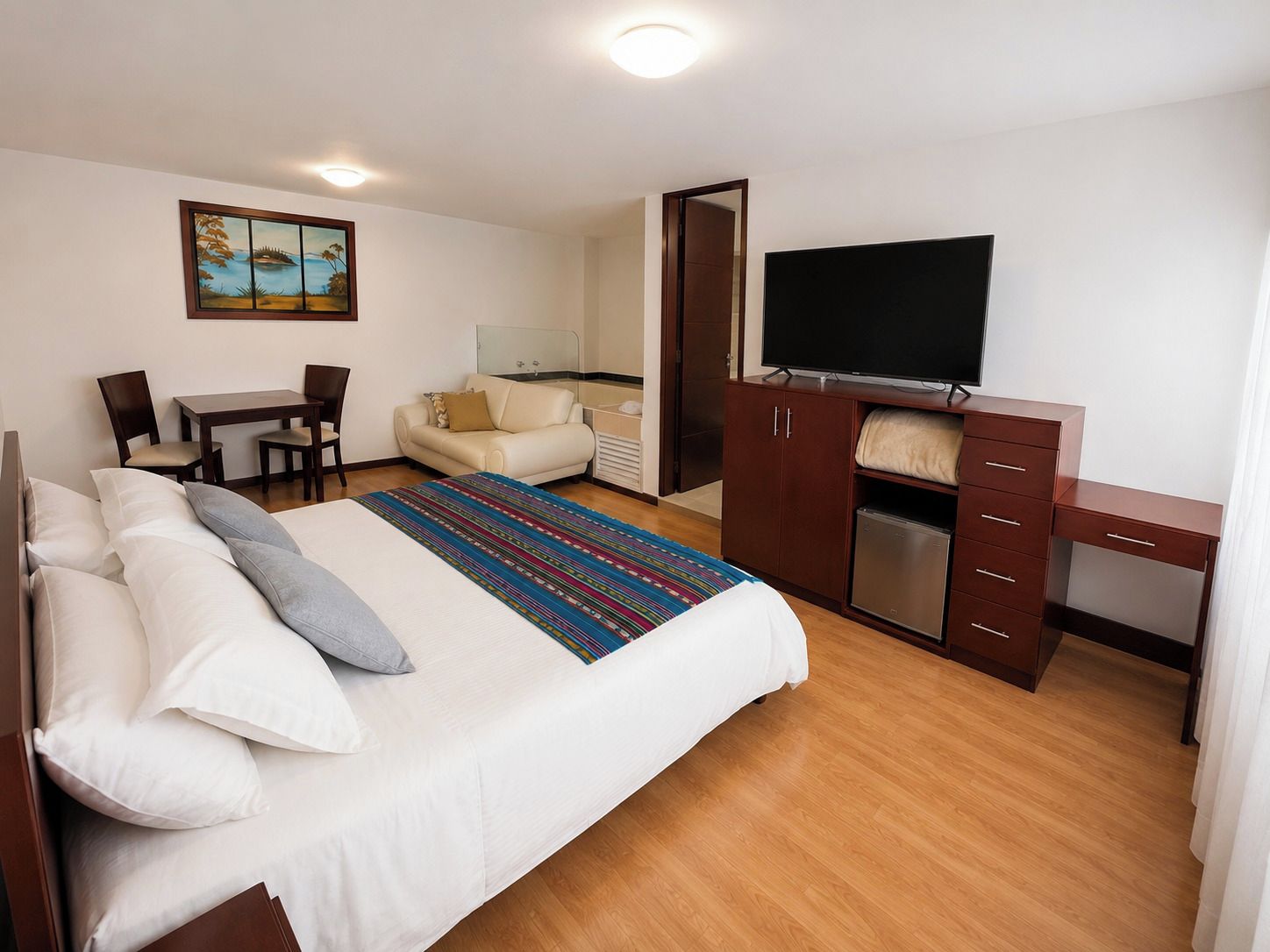 Una habitación de hotel con una cama, un escritorio, un televisor y un cuadro en la pared.