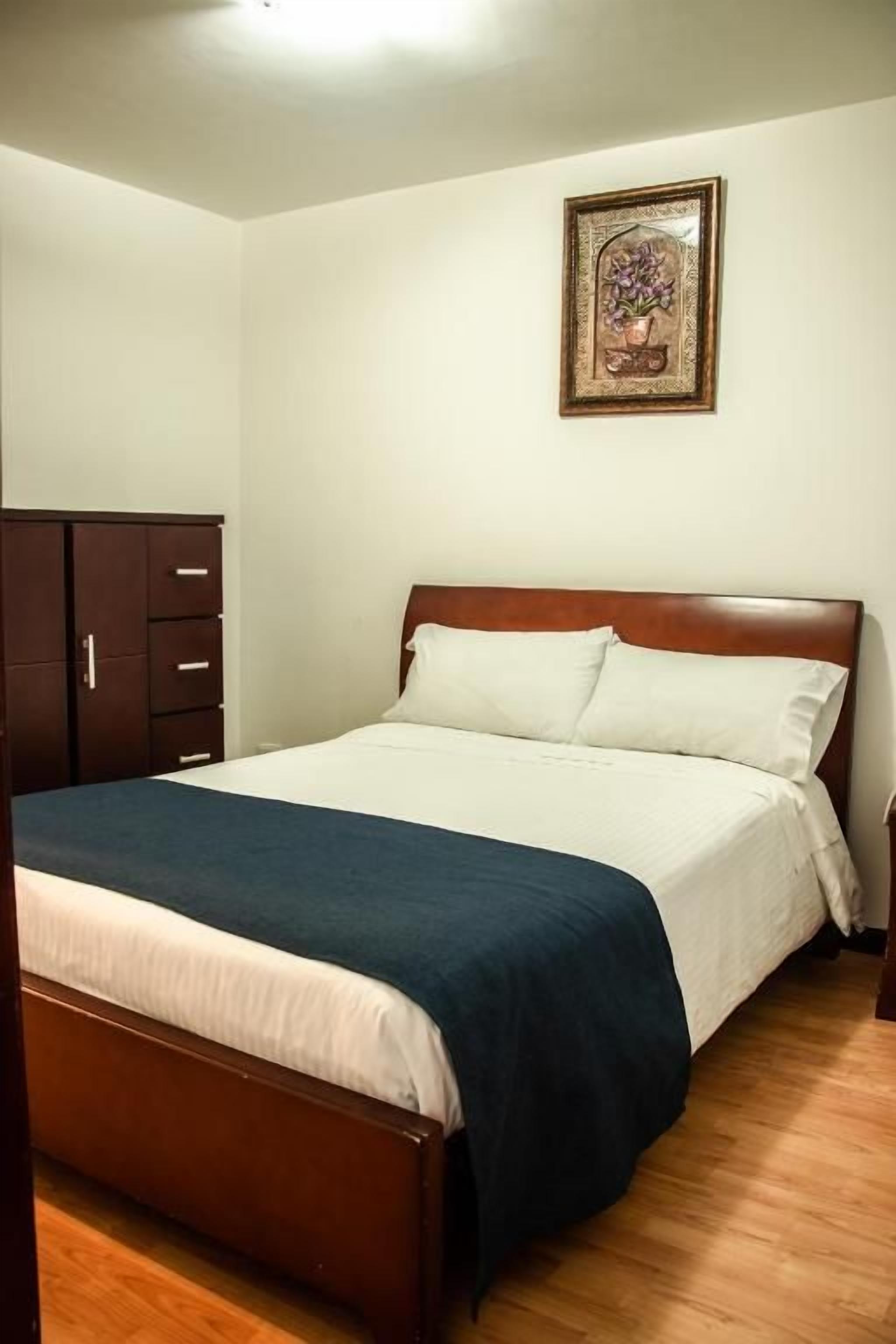 A bedroom with a bed, wooden headboard, a dresser, and a framed picture on the wall.