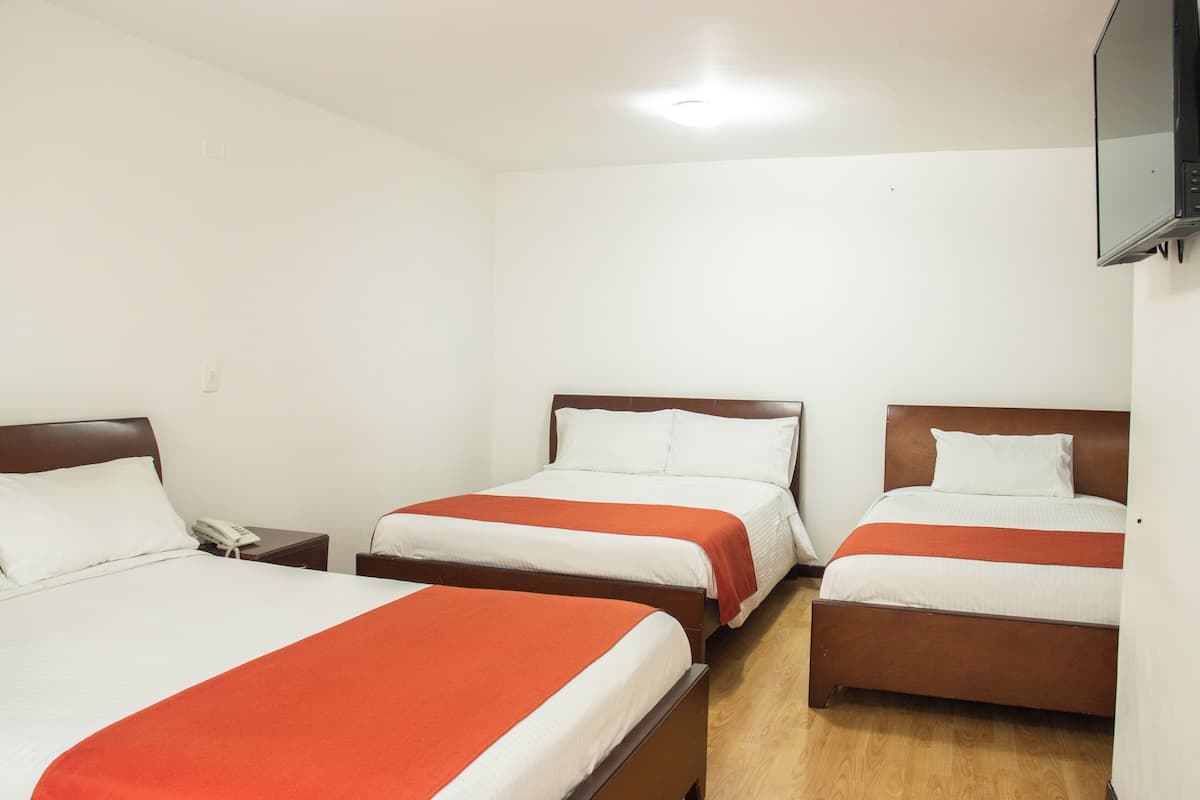 Ett hotellrum med tre sängar, var och en med en sänggavel i trä och vitt sänglinne. En platt-TV är monterad på väggen.