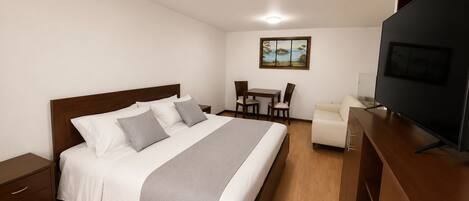 Habitación de hotel con cama, escritorio, silla, televisor y un cuadro en la pared.