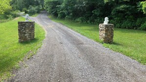 Un camino de grava bordeado por pilares de piedra con estatuas, rodeado de abundante vegetación.