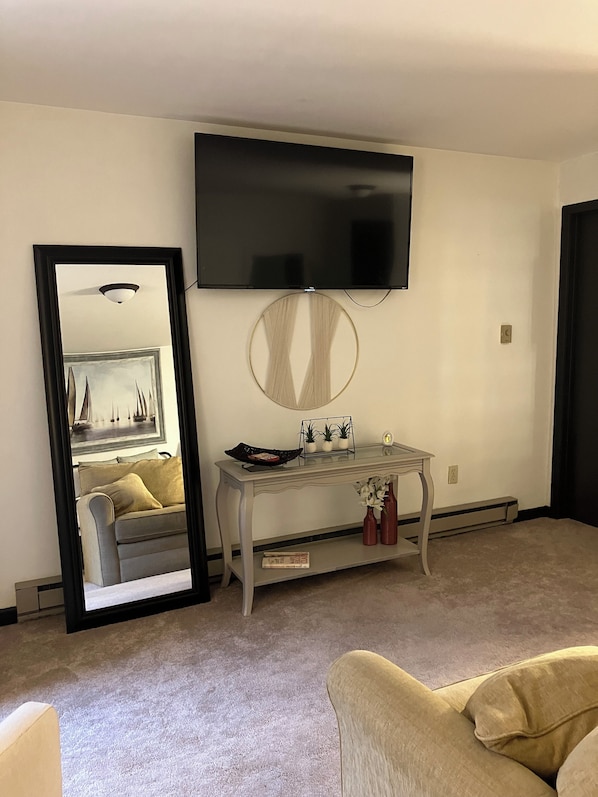 Un salon avec un téléviseur à écran plat fixé au mur, un miroir rond, une petite table agrémentée d’objets décoratifs et un canapé.