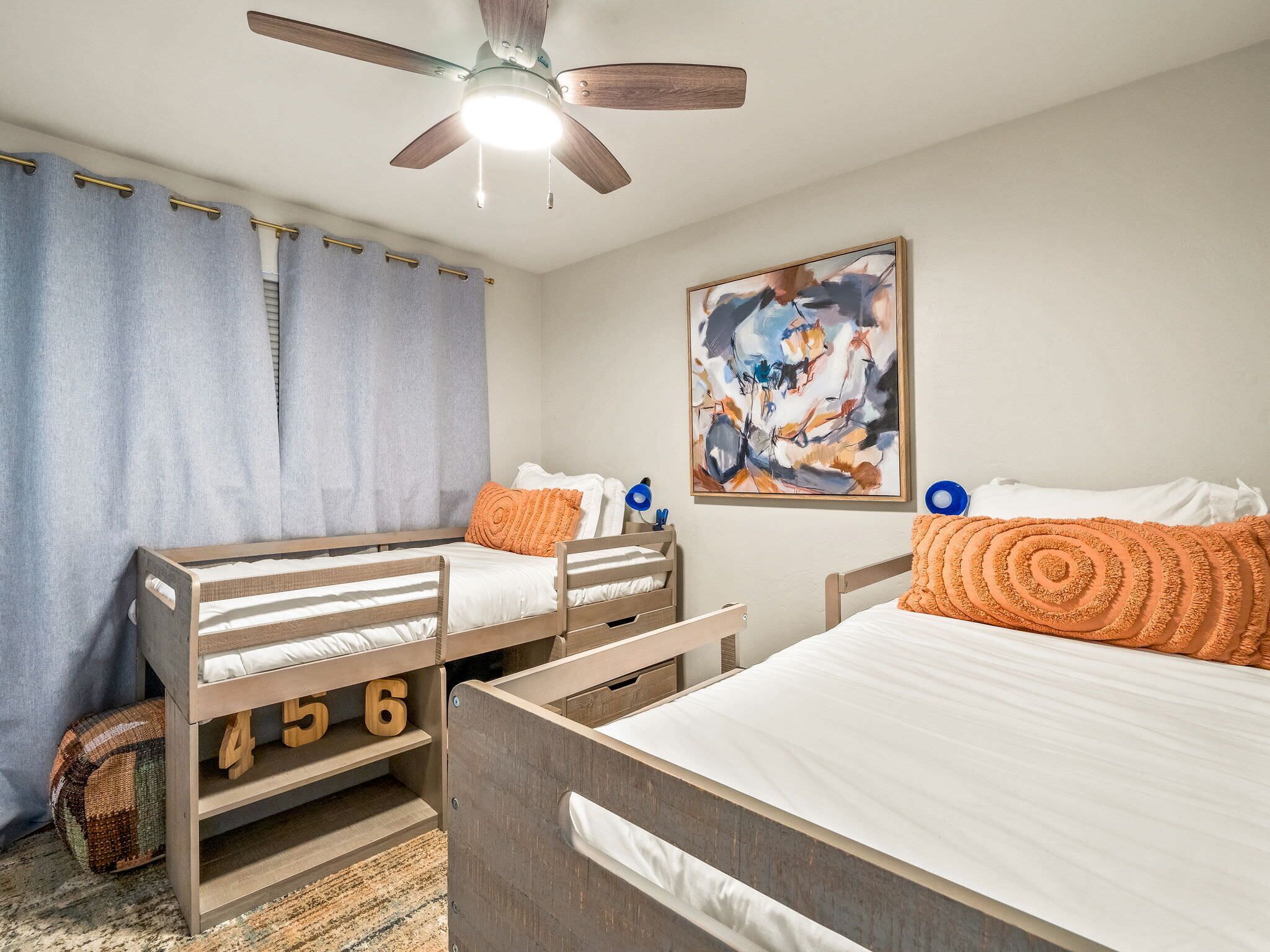 Une chambre avec deux lits superposés, un ventilateur de plafond, un tableau et un tapis.