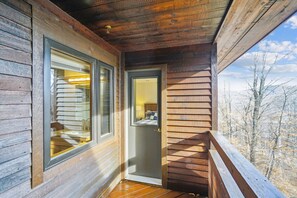 A wooden cabin with a balcony, a door leading to a bedroom, and a view of trees.