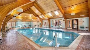 An indoor swimming pool with wooden beams and a brick floor, surrounded by lounge chairs and a view of the outdoors. - Inviting Two bedroom Two bathroom Highridge Condo B12 (Killington)