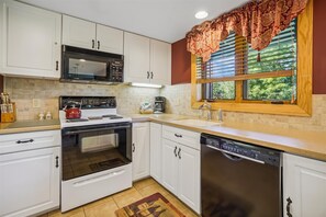 A kitchen with white cabinets, a microwave, stove, oven, and dishwasher. There's a window with blinds and a decorative valance. - 2-bedroom condo with private sauna, pool, and hot tub. (Killington)