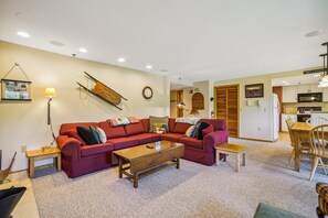 A living room with a red sofa, wooden coffee table, and a dining area with a wooden table and chairs. - 2-bedroom condo with private sauna, pool, and hot tub. (Killington)