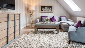 A modern loft bedroom with a sloped ceiling, a large window, a flat-screen TV, a wooden wardrobe, a coffee table with decorative items, and a grey sofa with purple cushions. - Aarnhorst App. 7 - Strandnahe, Moderne 2-zimmer Ferienwohnung auf 76 m² Wohnfläche, für 2 Personen (Wenningstedt-Braderup (Sylt))