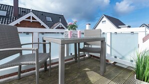 An outdoor patio with wicker furniture and a table, surrounded by a wooden deck and white fences. - Aarnhorst App. 7 - Strandnahe, Moderne 2-zimmer Ferienwohnung auf 76 m² Wohnfläche, für 2 Personen (Wenningstedt-Braderup (Sylt))