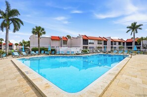 A swimming pool with lounge chairs and palm trees, surrounded by buildings with red roofs. - Watch dolphins & pelicans from this 2 bedroom/2 bath waterfront condo. (Bradenton Beach)