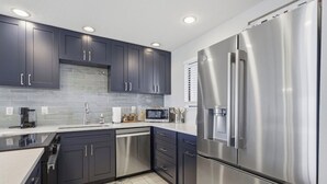 A modern kitchen with dark cabinets, stainless steel appliances, and a tiled backsplash.