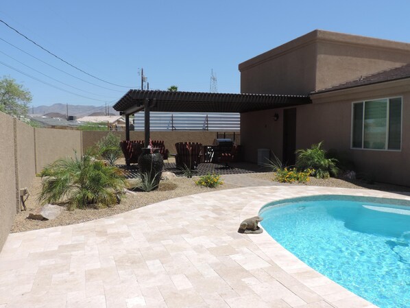 A backyard with a swimming pool, patio furniture, and a covered outdoor seating area.