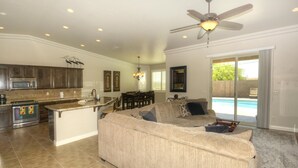 A spacious living area with a large beige sectional sofa, a kitchen with dark wood cabinets, and a view of the beach through a sliding glass door. - Sunny Ridge Elegance (Lake Havasu City)
