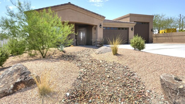 A modern two-story house with a beige exterior, a garage, and a landscaped front yard with rocks and sparse vegetation. - Sunny Ridge Elegance (Lake Havasu City)