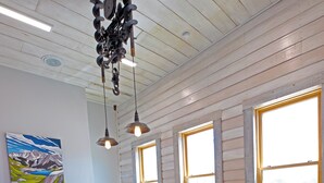 A spacious dining area with a long table and multiple chairs, large windows with natural light, and a ceiling fan.